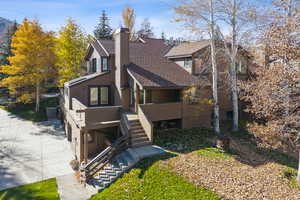 View of front of property featuring roof with shingles, stairway, a chimney, and a wooden deck