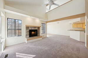 Unfurnished living room with light colored carpet, high vaulted ceiling, a tiled fireplace, and ceiling fan