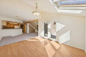 Foyer with stairway, light wood finished floors, lofted ceiling, french doors, and a skylight