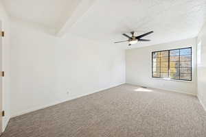 Carpeted empty room featuring beamed ceiling, a ceiling fan, and a textured ceiling
