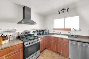 Kitchen featuring stainless steel appliances, wall chimney exhaust hood, brown cabinetry, dark countertops, and a textured ceiling