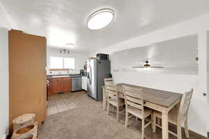 Kitchen with a textured ceiling, appliances with stainless steel finishes, light carpet, light tile patterned floors, and brown cabinetry