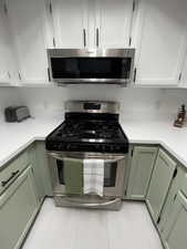Kitchen with green cabinetry, stainless steel appliances, white cabinets, and light countertops