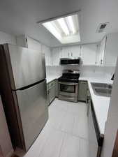 Kitchen featuring appliances with stainless steel finishes, white cabinetry, green cabinets, and light countertops