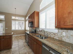 Kitchen featuring stainless steel appliances, dark stone countertops, suspended lighting, vaulted ceiling, and backsplash