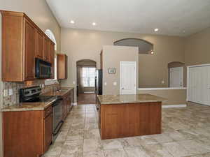 Kitchen with stainless steel appliances, arched walkways, wood finish cabinets, a center island, and a high ceiling