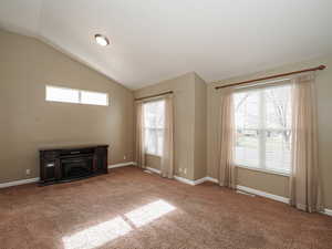 Unfurnished living room with carpet, a glass covered fireplace, and vaulted ceiling