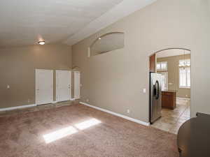 Unfurnished room with light carpet, vaulted ceiling, arched walkways, light tile patterned flooring, and suspended lighting
