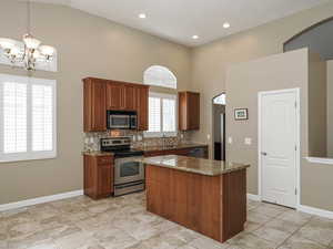 Kitchen with stainless steel appliances, arched walkways, a kitchen island, dark stone countertops, and decorative backsplash
