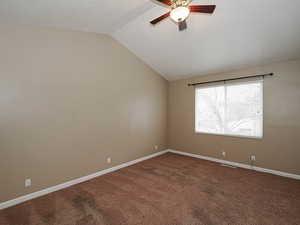 Empty room with a ceiling fan, dark carpet, and vaulted ceiling