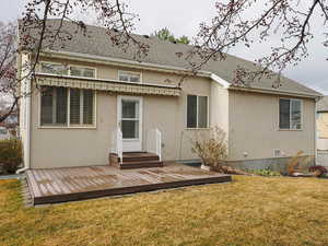 Back of property with a lawn, stucco siding, a deck, and a shingled roof