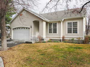 View of front of property with a front yard, stucco siding, an attached garage, driveway, and roof with shingles