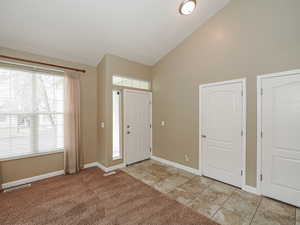 Foyer entrance featuring vaulted ceiling and light colored carpet