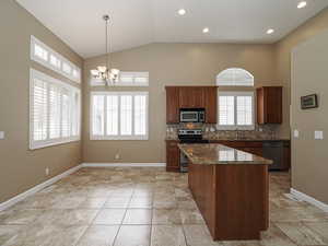 Kitchen featuring stainless steel appliances, dark stone countertops, decorative backsplash, a chandelier, and vaulted ceiling
