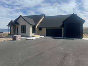 Modern farmhouse with stone siding, an attached garage, asphalt driveway, and roof with shingles