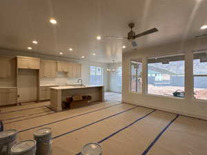 Kitchen featuring ceiling fan, a chandelier, a kitchen island with sink, and light stone counters