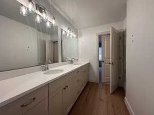 Bathroom with double vanity, dark wood finished floors, and a textured ceiling