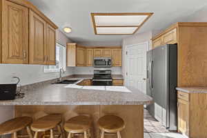 Kitchen featuring a peninsula, appliances with stainless steel finishes, a breakfast bar area, light countertops, and brown cabinetry