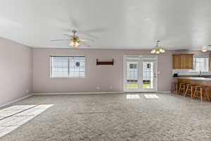 Unfurnished living room with a chandelier, light colored carpet, and a ceiling fan