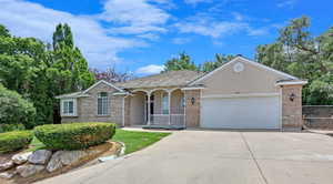 Stucco and brick exterior featuring an arched portico entryway with white railings, a two-car garage, mature landscaping, and a concrete driveway