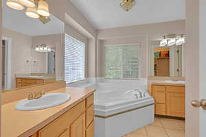 Bathroom featuring light tile patterned floors, a garden tub, and two vanities