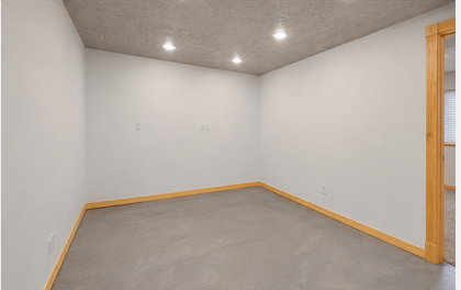 Recessed lighting illuminates this room featuring concrete flooring, light wood-finish baseboards, and a doorway with a light wood-finish frame