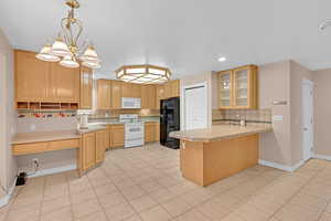 Kitchen featuring backsplash, a peninsula, glass insert cabinets, white appliances, and recessed lighting