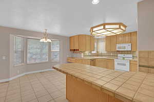 Kitchen featuring tile counters, white appliances, light brown cabinets, tasteful backsplash, and light tile patterned floors