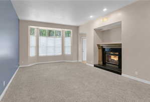 Spacious living area featuring a bay window, recessed lighting, and an integrated fireplace with a dark stone hearth and mantel