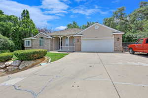 Ranch-style home featuring brick siding, a porch, driveway, a garage, and stucco siding