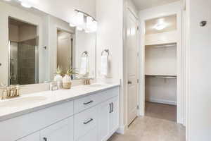 Bathroom featuring a shower stall, double vanity, light tile patterned floors, and a spacious closet