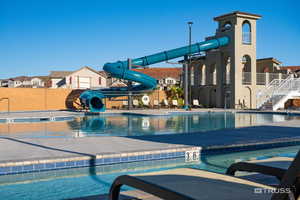 Community pool with a water slide, stairs, and a patio area