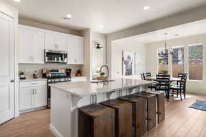 Kitchen with appliances with stainless steel finishes, light wood-type flooring, a breakfast bar area, white cabinets, and light stone counters