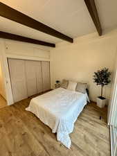 Bedroom with light wood finished floors, beam ceiling, and a closet