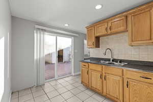 Kitchen with dark countertops, decorative backsplash, recessed lighting, light tile patterned floors, and brown cabinetry