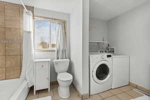 Bathroom featuring light tile patterned flooring, shower / tub combo with curtain, and separate washer and dryer