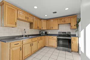 Kitchen featuring stainless steel appliances, dark countertops, light tile patterned floors, recessed lighting, and tasteful backsplash