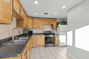 Kitchen with appliances with stainless steel finishes, dark countertops, light tile patterned floors, recessed lighting, and decorative backsplash