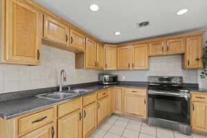 Kitchen featuring stainless steel appliances, dark countertops, light tile patterned flooring, tasteful backsplash, and recessed lighting