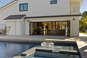Rear view of property featuring a standing seam roof, a metal roof, board and batten siding, and a pool with connected hot tub