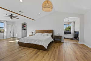 Bedroom with arched walkways, light wood-style flooring, vaulted ceiling, and recessed lighting
