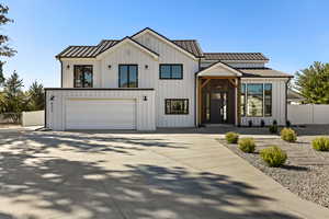 Modern inspired farmhouse with a metal roof, a standing seam roof, board and batten siding, and driveway
