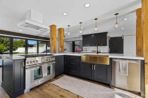Kitchen featuring stainless steel appliances, recessed lighting, light wood-type flooring, a peninsula, and custom range hood
