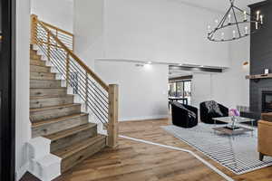 Staircase with a towering ceiling, wood finished floors, a large fireplace, and a chandelier