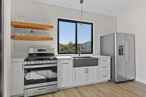 Kitchen featuring white cabinetry, appliances with stainless steel finishes, open shelves, decorative light fixtures, and light wood-type flooring