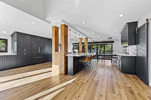 Kitchen featuring dark cabinets, a kitchen bar, light wood finished floors, recessed lighting, and light stone countertops