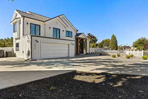 Modern farmhouse featuring board and batten siding, driveway, a metal roof, and a garage