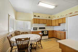 Kitchen featuring white appliances, light countertops, crown molding, light wood-style floors, and brown cabinets