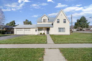 Traditional-style house with covered porch, a metal roof, a front lawn, a garage, and driveway