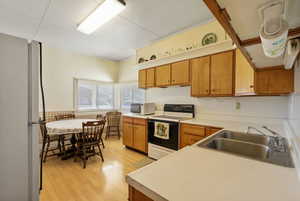 Kitchen with white appliances, light countertops, brown cabinets, light wood-style flooring, and ornamental molding